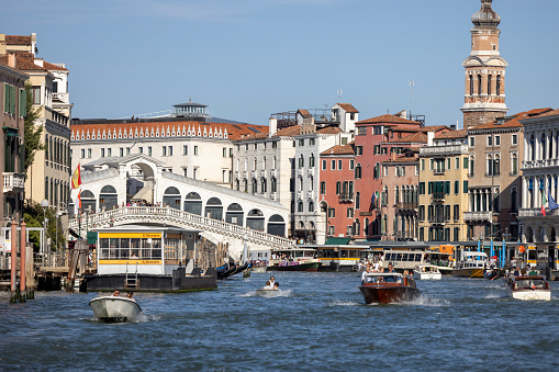 Venice, Italy - September 27, 2023: Grand Canal, historic decorative tenement houses by the water, floating boats. Rialto Bridge (Ponte de Rialto) in a distance