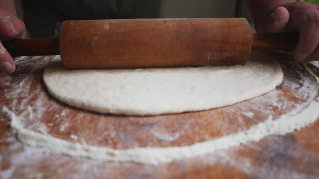 A young housewife kneads yeast dough on a wooden board.