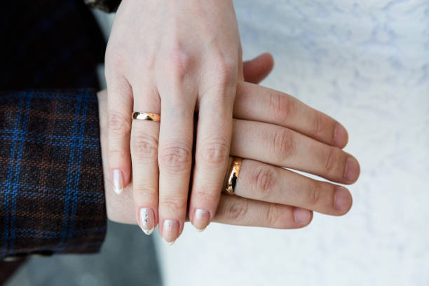 istock Interlaced hands with golden wedding rings. Focus on intricate ring designs, signifying love and commitment, against a soft white background. 1763462331