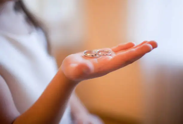 Photo of Close-up of a child's hand cradling intertwined wedding rings, bathed in soft light, evoking sentiments of innocence and cherished moments.