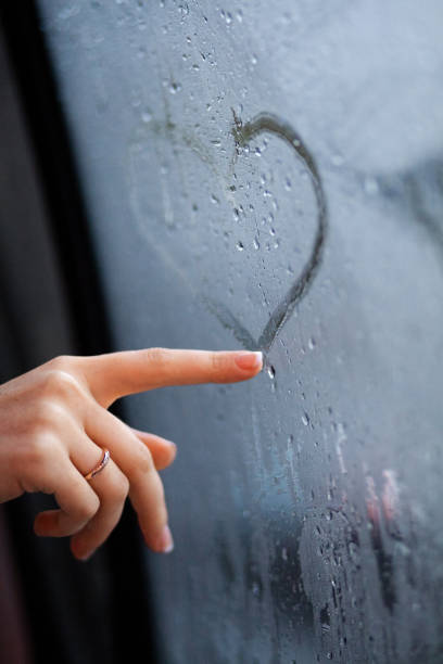 istock A woman's hand with a ring traces a heart on a misted window, amidst raindrops; a sharp-focus evokes fleeting emotions of love and longing. 1763480218