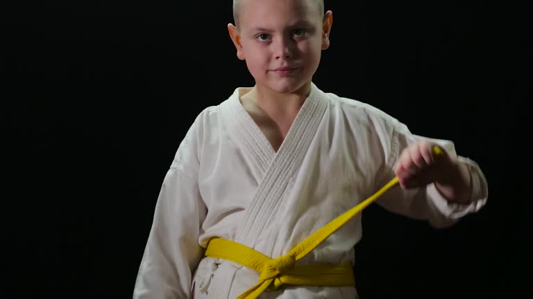 A plump athlete with a yellow belt ties a belt on a black background