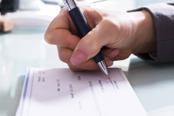 Businessperson Signing Cheque In Office Close-up Of A Businessperson's Hand Signing Cheque With Pen In Office Plagiarism Checkers stock pictures, royalty-free photos & images