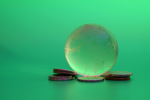 A glass globe with coins on a green background. Financial symbol.