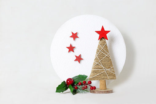 Simple Christmas tree made with strings on white background. Stars are made of red wood. Wooden base. There's sprig of holly and white moon behind tree. Horizontal.