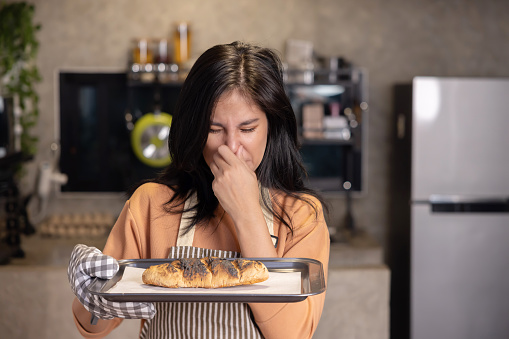 Upset Asian Woman Look at the Her Overcooked Burnt Bread from the Oven