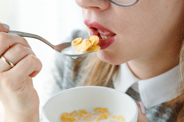 Closeup of mouth-eating corn flakes with milk on breakfast, unrecognizable woman. stock photo