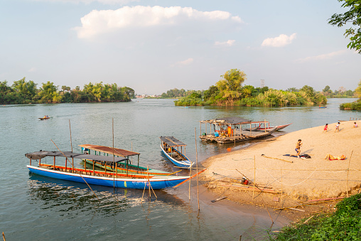 ,4000 Islands,Si Phan Don, Khong District,Laos-February 21 2023: Travelers relax on the tiny Mekong River beach ,small wooden boats ferry people to and from Nakasong and Don Som Islands to here.