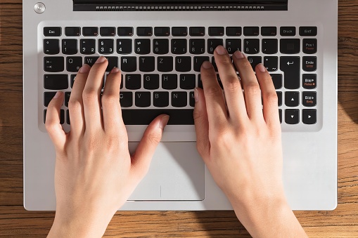 Close-up Of A Person Using Laptop Computer On Office Wooden Desk