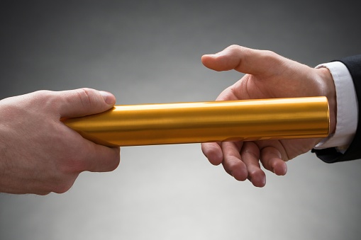 Close-up Of Two Businessman's Hand Passing A Golden Relay Baton