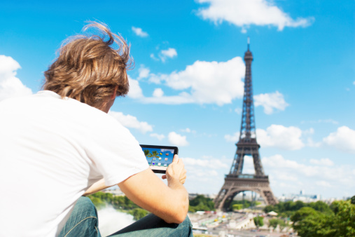 A male guy, having a look at his tablet PC in front of the fantastic Eiffel-Tower in Paris, France. Maybe he is checking weather information.