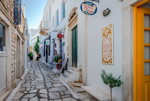 Pyrgos, Greece - September 22 2023: Narrow alley with whitewashed traditional houses and shops on both sides. Pyrgos is the biggest and most charming village in Tinos Island, Cyclades.