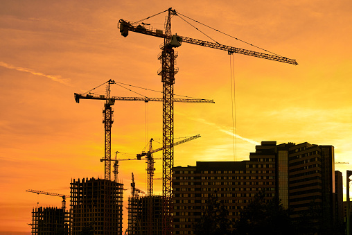 Tower cranes silhouette and high-rise buildings under construction at construction site against yellow sunset. Shooting the building new houses in the city