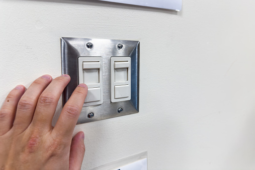 Close up of finger is turning on light switch with blue wall
