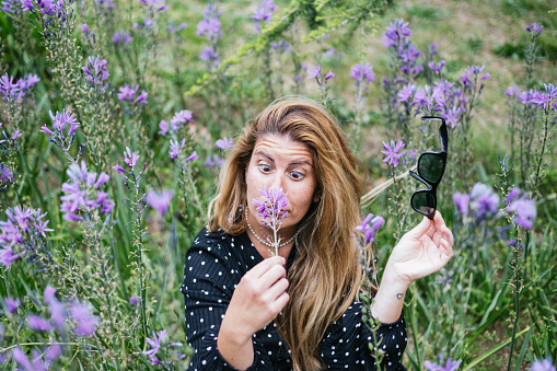 mature blonde woman smelling a violet flower being allergic.