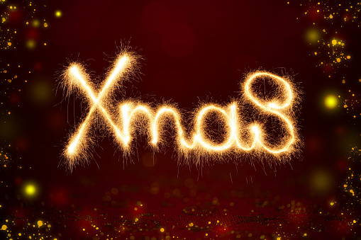 Xmas lettering made by sparkler trace on a red festive background with defocused glowing lights.