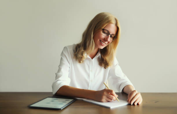 istock Professional young woman employee while working with digital tablet computer, writes something with pen on paper document sitting at the desk at home or office 1763858689