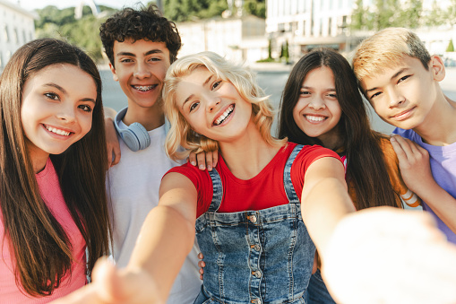 Group of smiling friends, multiracial teenagers taking selfie looking at camera on urban street. Young happy blogger influencer recording video standing together with friends. Summer concept