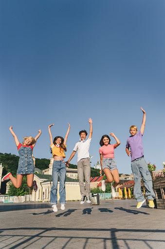 Portrait of smiling teenagers, children wearing stylish casual clothes, colorful t shirts jumping on urban street. Happy college students, friends meeting together. Positive lifestyle concept