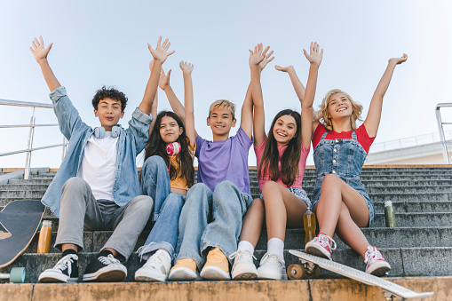 Group of happy friends, teenagers boys and girls in colorful t shirts holding hands up celebration summer vacation sitting on stairs
