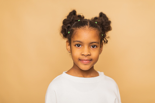 Close up head shot portrait of little brown-haired child girl. Cheerful kid against white studio wall background