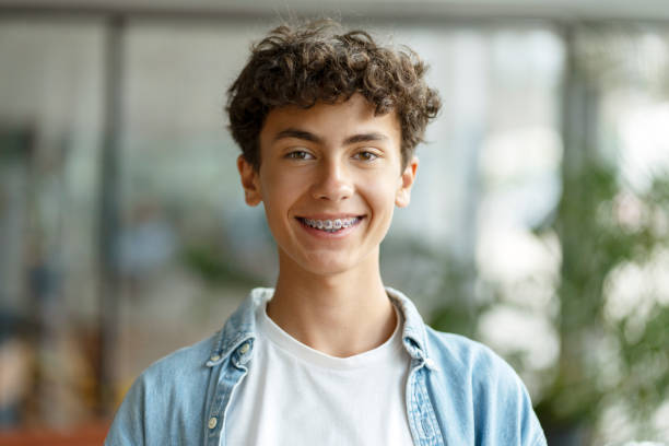 Portrait of smiling smart school boy wearing braces on teeth looking at camera. Education concept Closeup portrait of smiling smart curly haired school boy wearing braces on teeth looking at camera. Education concept brace stock pictures, royalty-free photos & images