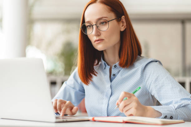 istock Pensive woman writing in notebook using laptop sitting at workplace outdoors working online 1763927047