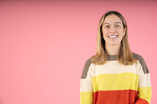 Happy young woman smiling looking at the camera, on a pink background.