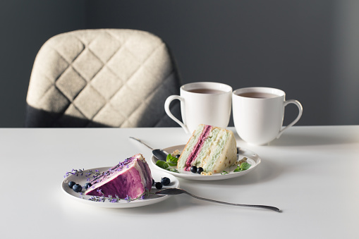 berry cheesecakes and two cups of tea on  white table on background gray wall