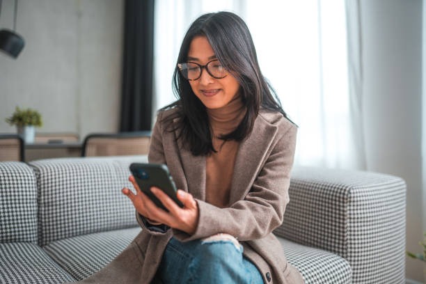 istock Beautiful Young Woman Scroling Through Phone Sitting On Couch 1764036711
