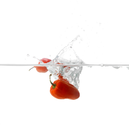 Whole red, green and yellow bell peppers falling into water with a black background creating bubbles and a splash