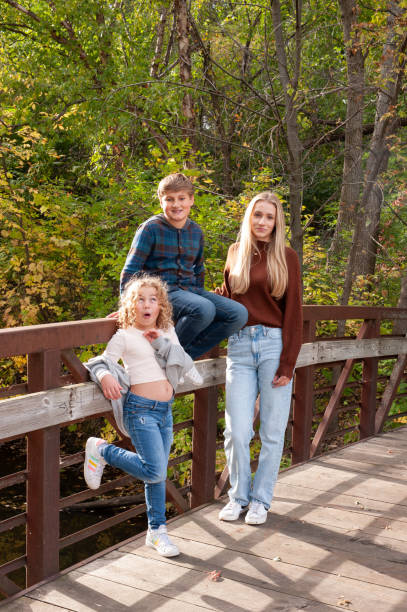 istock Blending Families: three kids lean/sit against a quaint metal bridge railing during the fall season. 1764129842