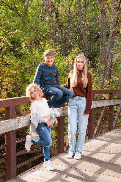istock Blending Families: three kids lean/sit against a quaint metal bridge railing during the fall season. 1764129850