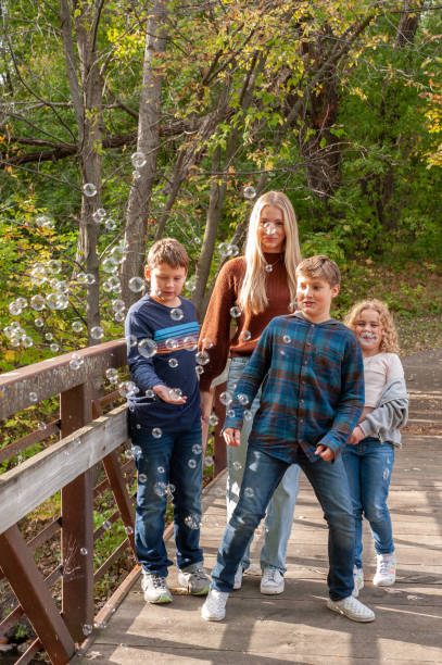 istock Blending Families: four kids chase bubbles on a quaint bridge during the fall season. 1764130934