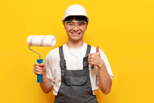 istock asian guy painter in uniform holds roller and shows like on yellow isolated background 1764141352