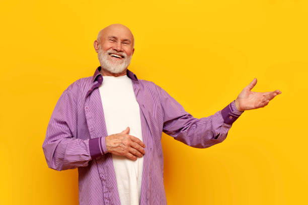 istock old bald grandfather with gray beard points to the side and laughs on yellow isolated background 1764145614