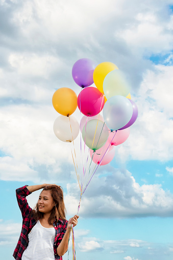 Cheerful cute girl holding balloons running on green meadow white cloud and blue sky with happiness. Hands holding vibrant air balloons play on birthday party happy times summer on sunlight outdoor