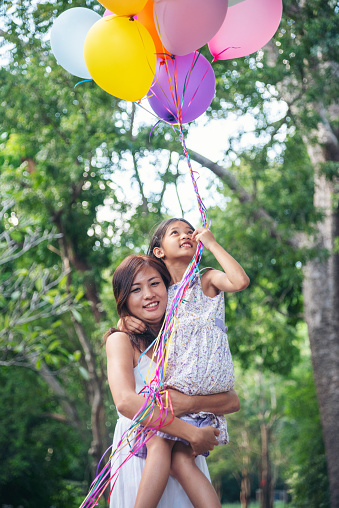 Vertical Happiness mother daughter play balloons together green garden park outdoor lifestyle. Happy family two people enjoy have fun cheerful. Mother childhood hand holding colorful balloons outside