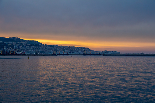 Beautiful panoramic view of the bay of Algiers, Alger, Algeria, from the beach at dawn. Quiet evening atmosphere. City in the background. Orange and yellow sunset.