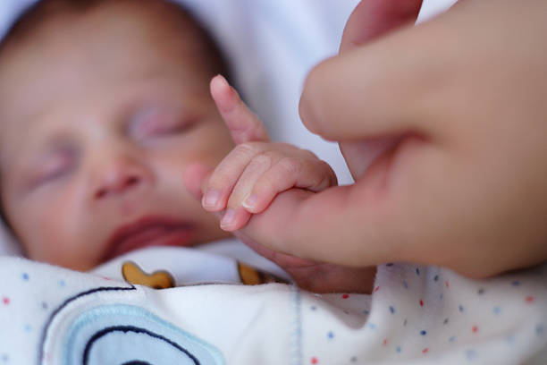 A newborn baby grasps his mother's hand.