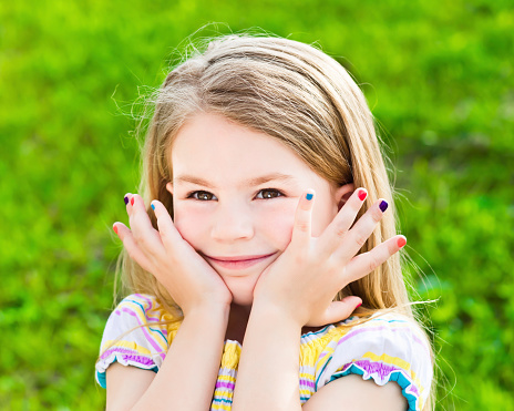 Cute smiling blond little girl with long hair and many-coloured manicure