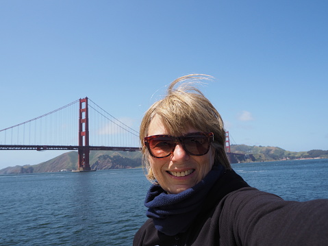 Smiling Woman 50+ in Front of Golden Gate Bridge and making Selfie