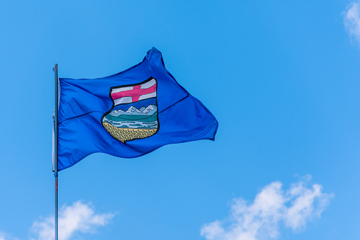 Canada Alberta provincial flag waving on a flagpole against blue sky background.