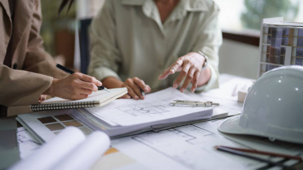 istock Two female architects discuss about interior design building project on blueprint and taking notes 1764271976