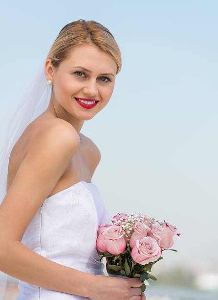 istock Beautiful Bride Holding Flower Bouquet Against Clear Blue Sky 176427476