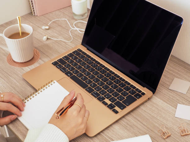 istock The hands of a woman taking notes while using a laptop at her desk, a feminine workspace, office and work-from-home concept with pastel pink and wood grain tones. 1764283109