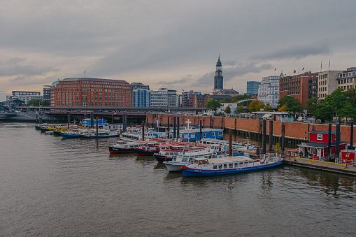 Hamburg, Germany - 25 October 2023: Modern buildings and boats on a canal in Kehrwieder with the bell tower of Michael Church in the background in Hamburg.