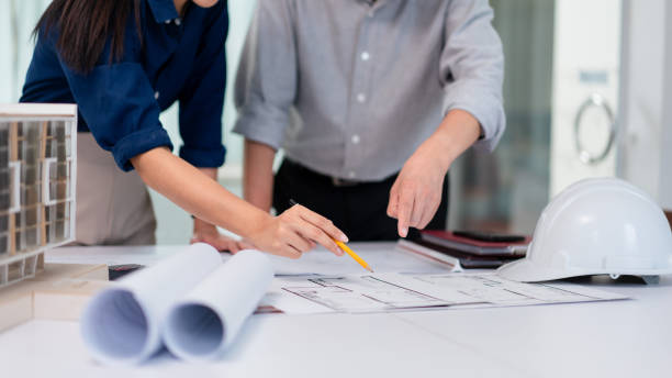 Two architects pointing on blueprint to discuss and planning about construction apartment project