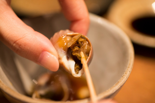 Whelk, which is a kind of edible sea snail, being eaten with a toothpick.