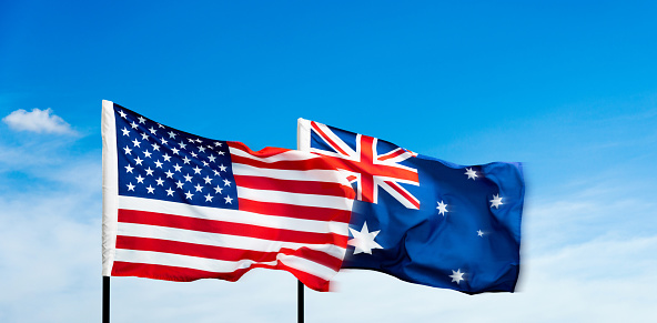 USA and Australia flags against blue sky background